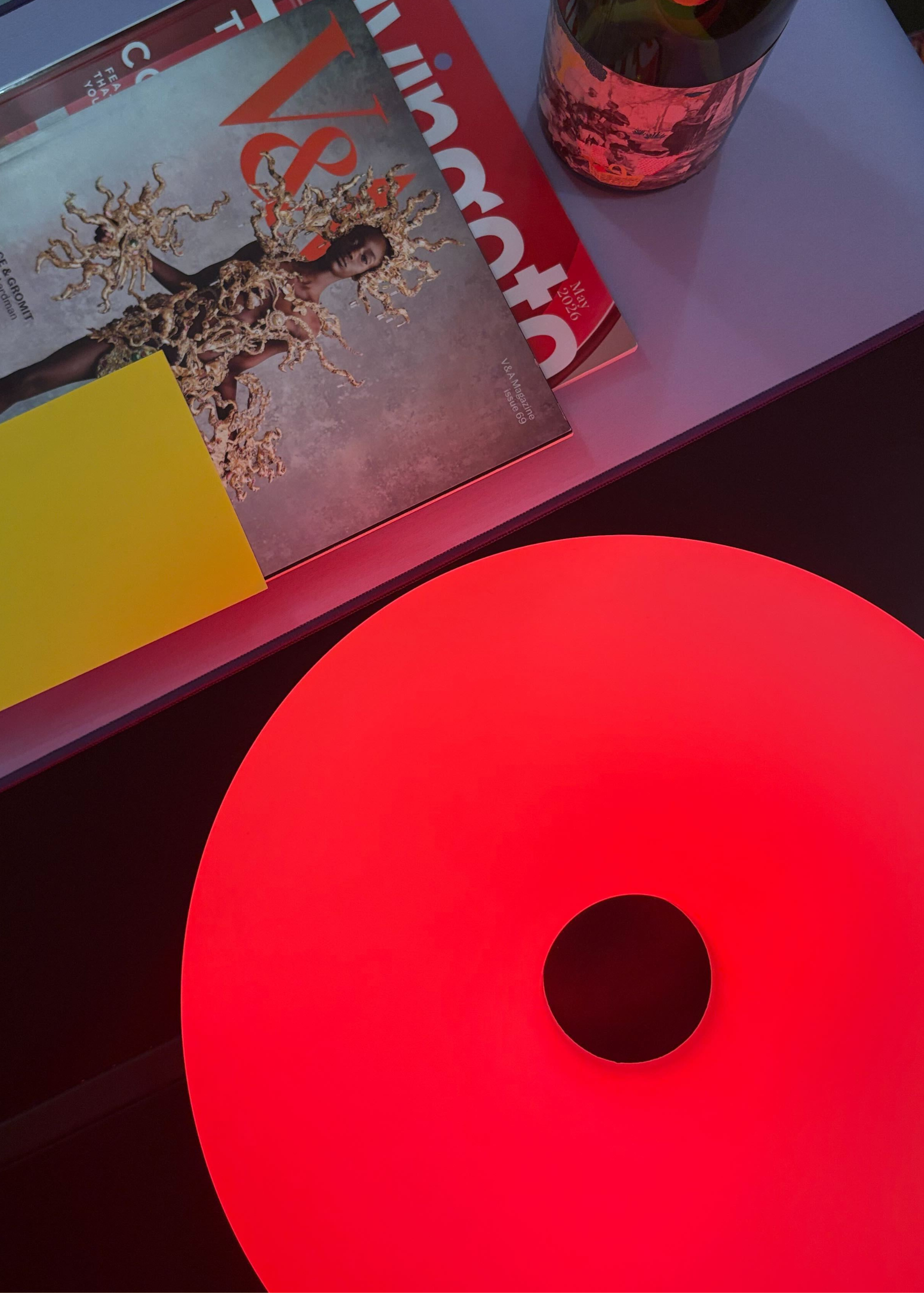 The IKEA VARMBLIXT donut lamp reflecting red light on a coffee table beside magazines