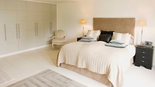 A minimalist bedroom in natural light with cream sheets and bedding, and two lit lamps on either of the bed