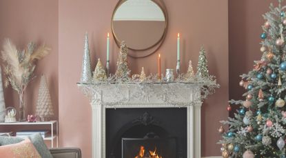 pink living room with pastel Christmas decorations, a white fireplace, pastel candles and a gold mirror