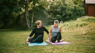 Two women laughing, sitting on yoga mats after practicing yoga for beginners in the garden