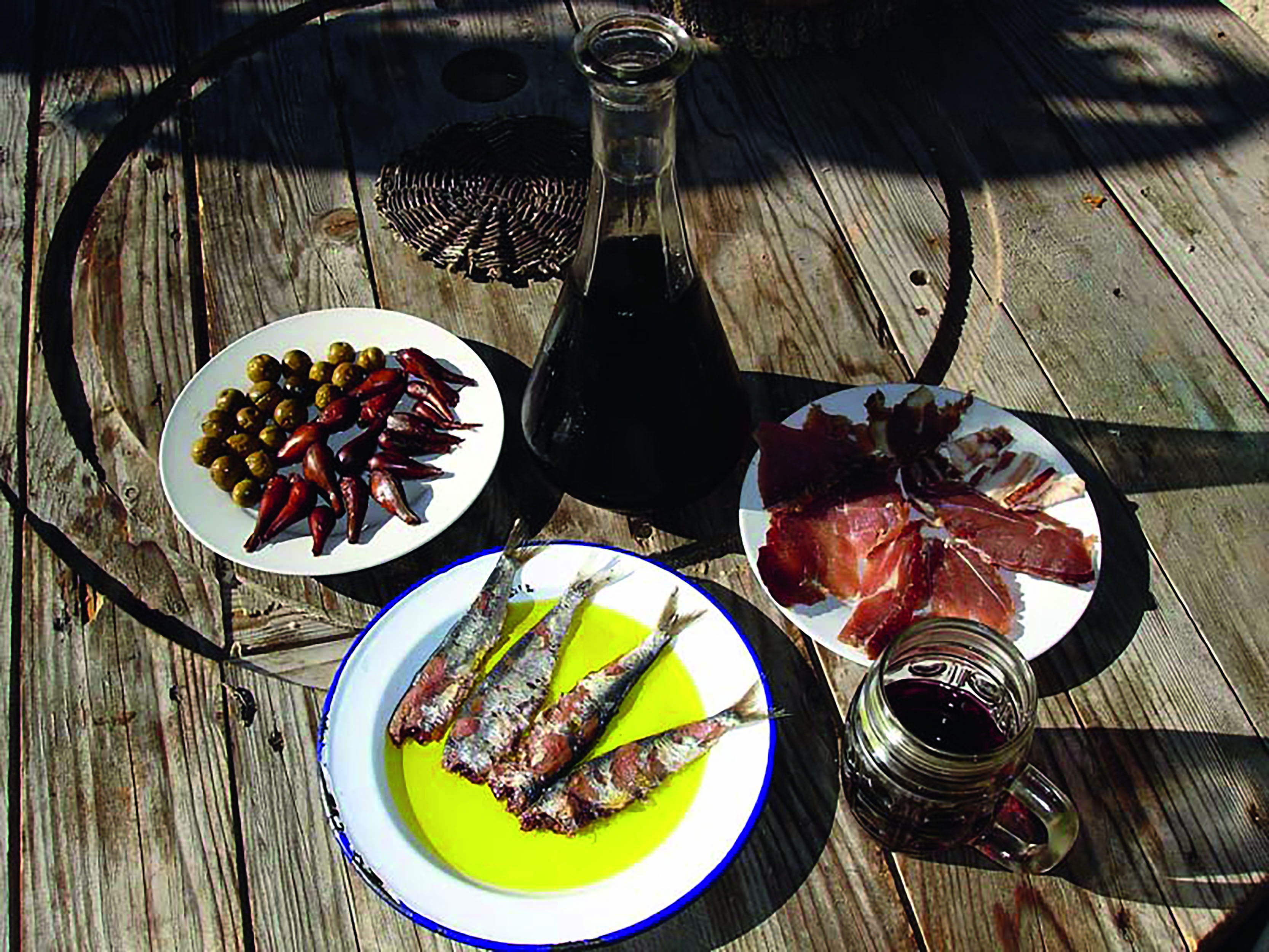 Plates on a wooden table with sardines in olive oil, slices of cured ham, olives and peppers