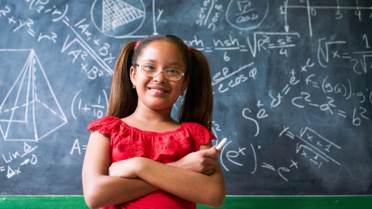 Smiling girl stands in front of blackboard filled with equations