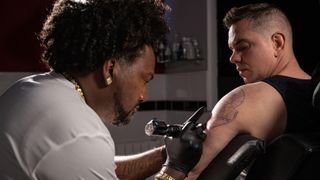 Professional African American tattoo artist makes a tattoo on client arm.