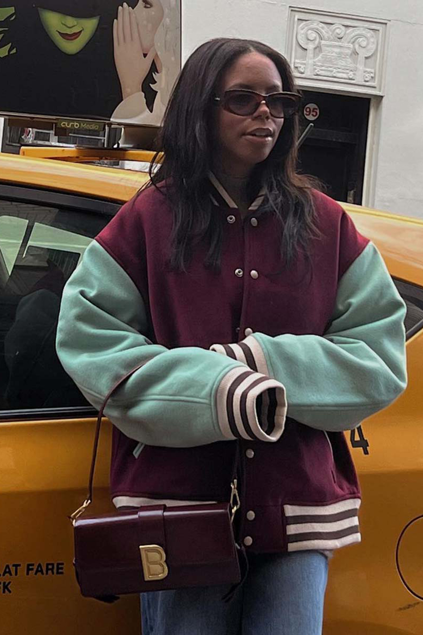 a woman wearing a burgundy and teal varsity jacket, jeans, and black bag