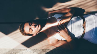 A woman relaxes in a meditative pose on a yoga mat.