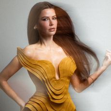 ariana madix poses with her hair wind swept as she wears a goldish yellow dress and poses with her hand on her hip