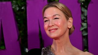 Image of Renée Zellweger smiling with blonde hair in a low bun and wearing a one-shoulder black dress