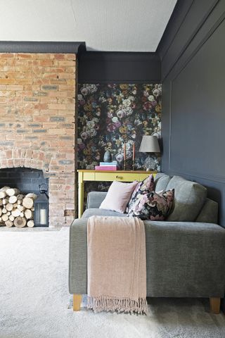 Black painted living room with light beige floor, grey sofa, wallpapered alcoves and brick fireplace wall