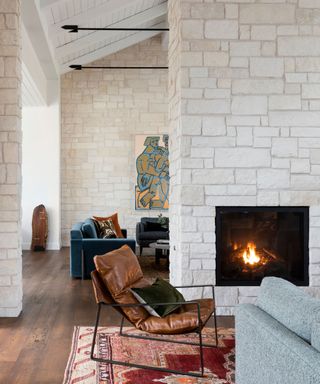 family room with bright rug leather chair and fire lit in stone fireplace with view to next room