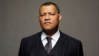 A press shot of Laurence Fishburne wearing a suit and looking directly into the camera