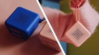 The pink and blue versions of IKEA's Vappeby Bluetooth speakers, on a pink table and being held on a string