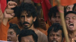 Dev Patel looks on angrily in a crowd of protestors