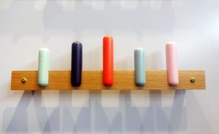 A coat rack with a wooden back and multicoloured straight hangers.