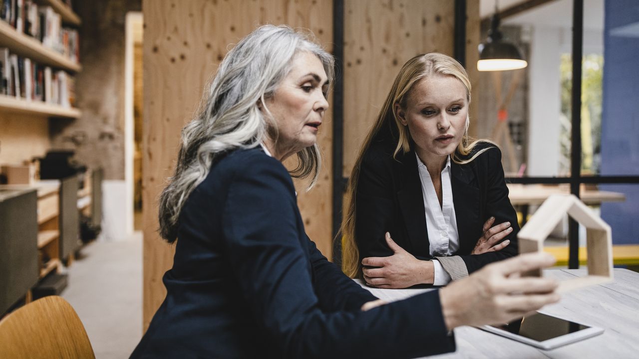 Mother-and-daughter business owners sit at a conference room table and look at a tablet.