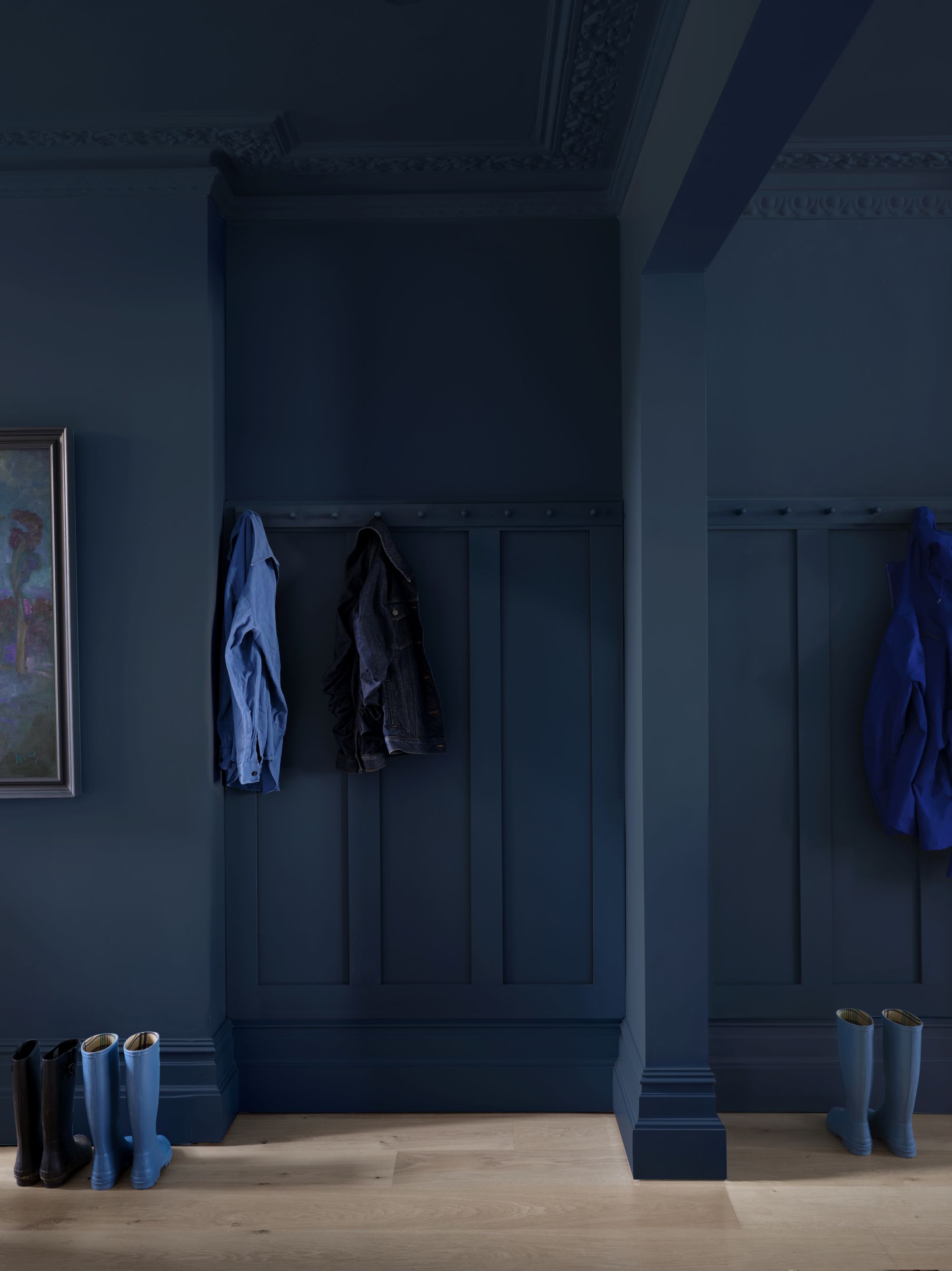 a blue-drenched mudroom with coats hanging on the wall and rainboots on the floor