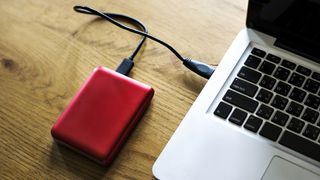 The best external hard drives: a red hard drive next to a MacBook 