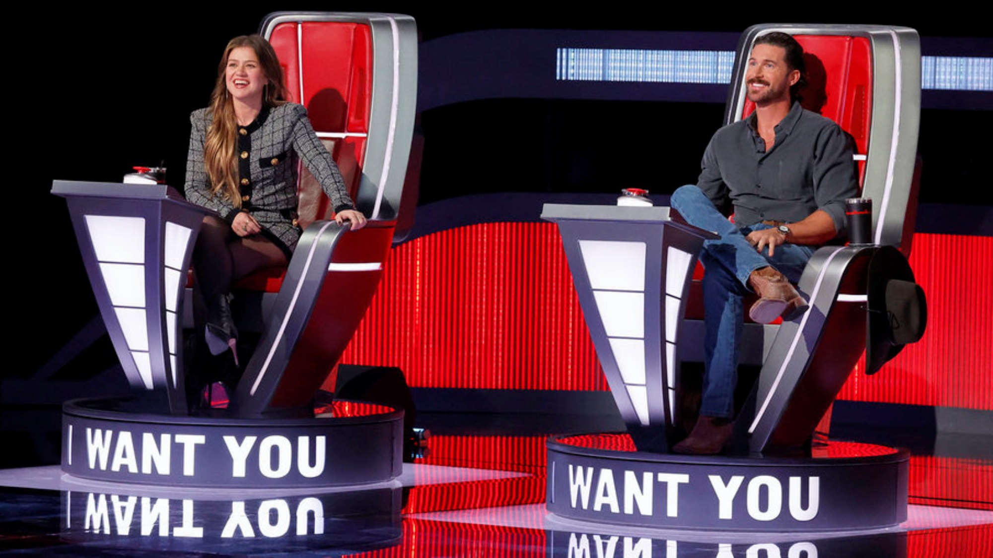 The Voice judges Kelly Clarkson and Riley Green sitting in their red chairs in Season 30.