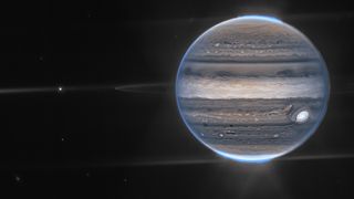 A composite image of Jupiter taken by Webb's NIRCam, showing the planet's rings and two of its moons, Amalthea and Adrastea. The blue glow around Jupiter's poles is the aurora.