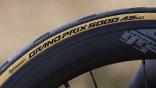 A tan-wall Continental Grand Prix 5000 AS TR tyre mounted to a black carbon rim