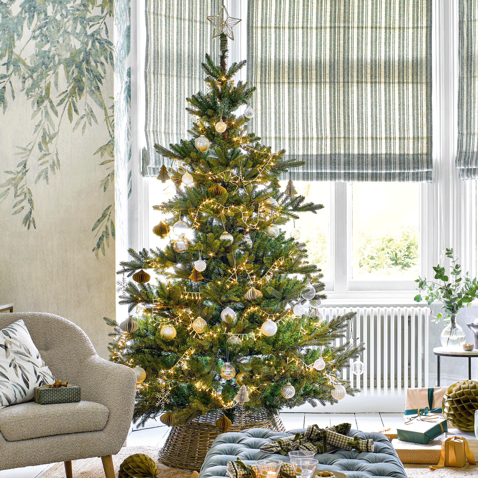 a pale green living room with a Christmas tree and a sofa, armchair and footstool