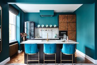 dark kitchen with wood effect cabinets, teal blue walls and velvet bar stools