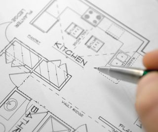 Computer-generated floorplans for a new house created by an architect. The plans show a kitchen with an hand and pen hoovering above.