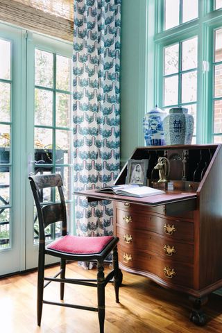 The corned of a teal room with an antique desk and chair