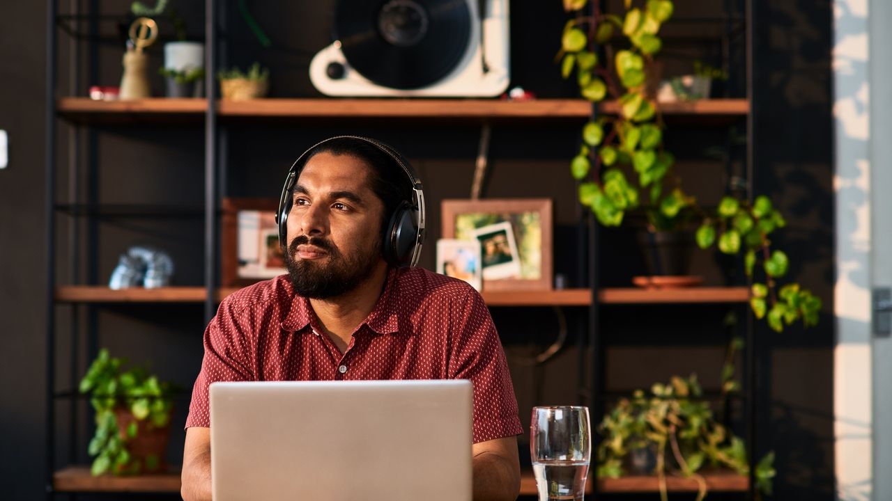 A man wearing headphones looks like he&#039;s considering something while sitting at his desk.