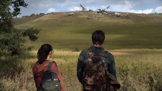 Bella Ramsey (as Ellie) and Pedro Pascal (as Joel) are seen from behind as they stare at a crashed plane in The Last of Us HBO series