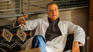 Harry Vanderspeigle (Alan Tudyk) dressed in a doctor's coat and holding a cigarette in "Resident Alien" Season 4 Episode 1.