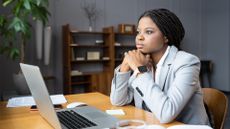 A distracted employee sitting at an office desk staring into space while working on a laptop computer.