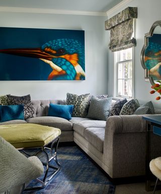 Living room with gray sectional with performance fabric, pillows and upholstered coffee table with large artwork of bird on wall