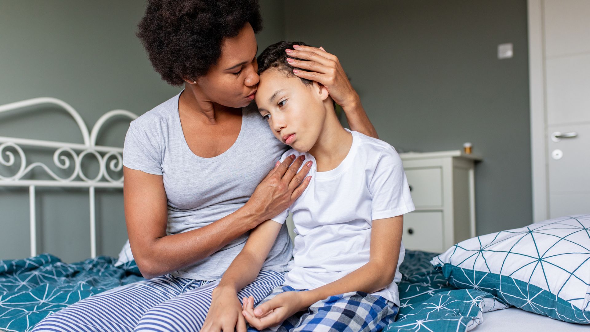 Mother comforting son at bedtime on a bed with blue bedding