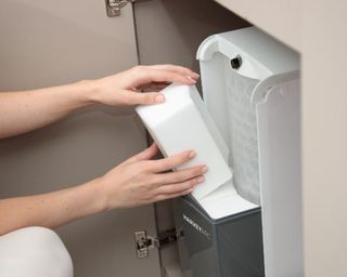A person using a water softener located under the kitchen sink