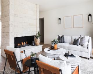 Fireplace hearth set in white modern stone in white lounge with accent leather chairs, a white striped couch and wall sconces