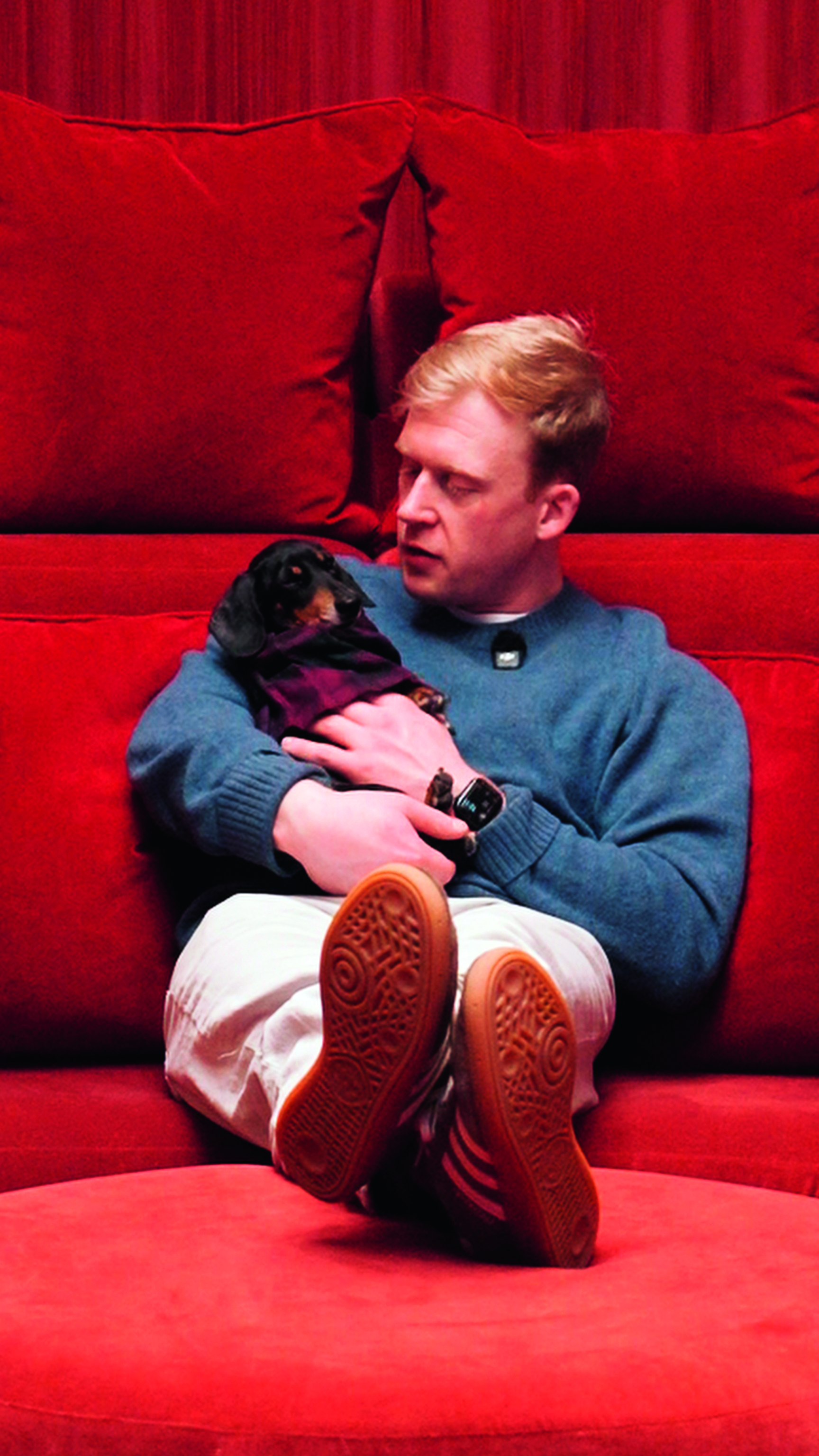 George Garrod holds Pizza the Queen, a dachshund, while reclining on a red sofa