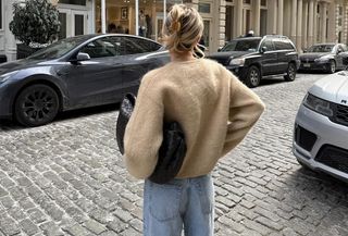 Woman wearing a Frame tan cardigan and light wash jeans.