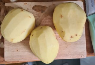 three peeled potatoes on a chopping board, ready to make chips