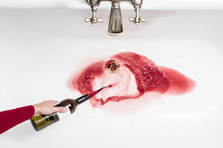 a woman throwing alcohol down the sink