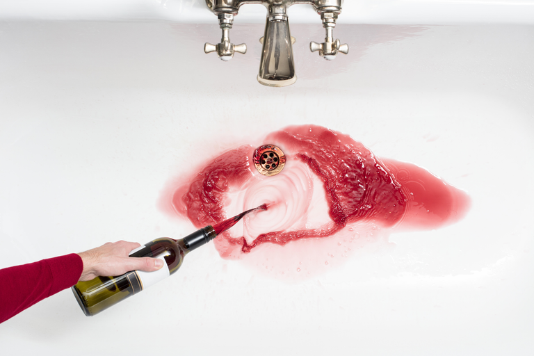 A woman not drinking alcohol by pouring red wine down the sink