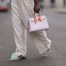 Woman wearing white trousers, green feathered shoes and a mini Hermes Birkin bag