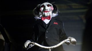 Billy the Puppet stands over the camera with a rope in his hands in the Saw movie