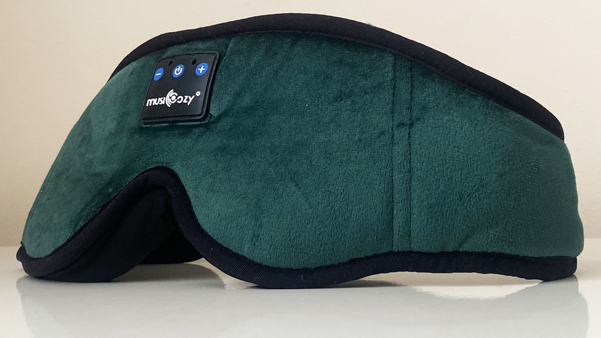 A closeup of the MUSICOZY Bluetooth Sleep Headphones Eye Mask in green on a white surface against a white background