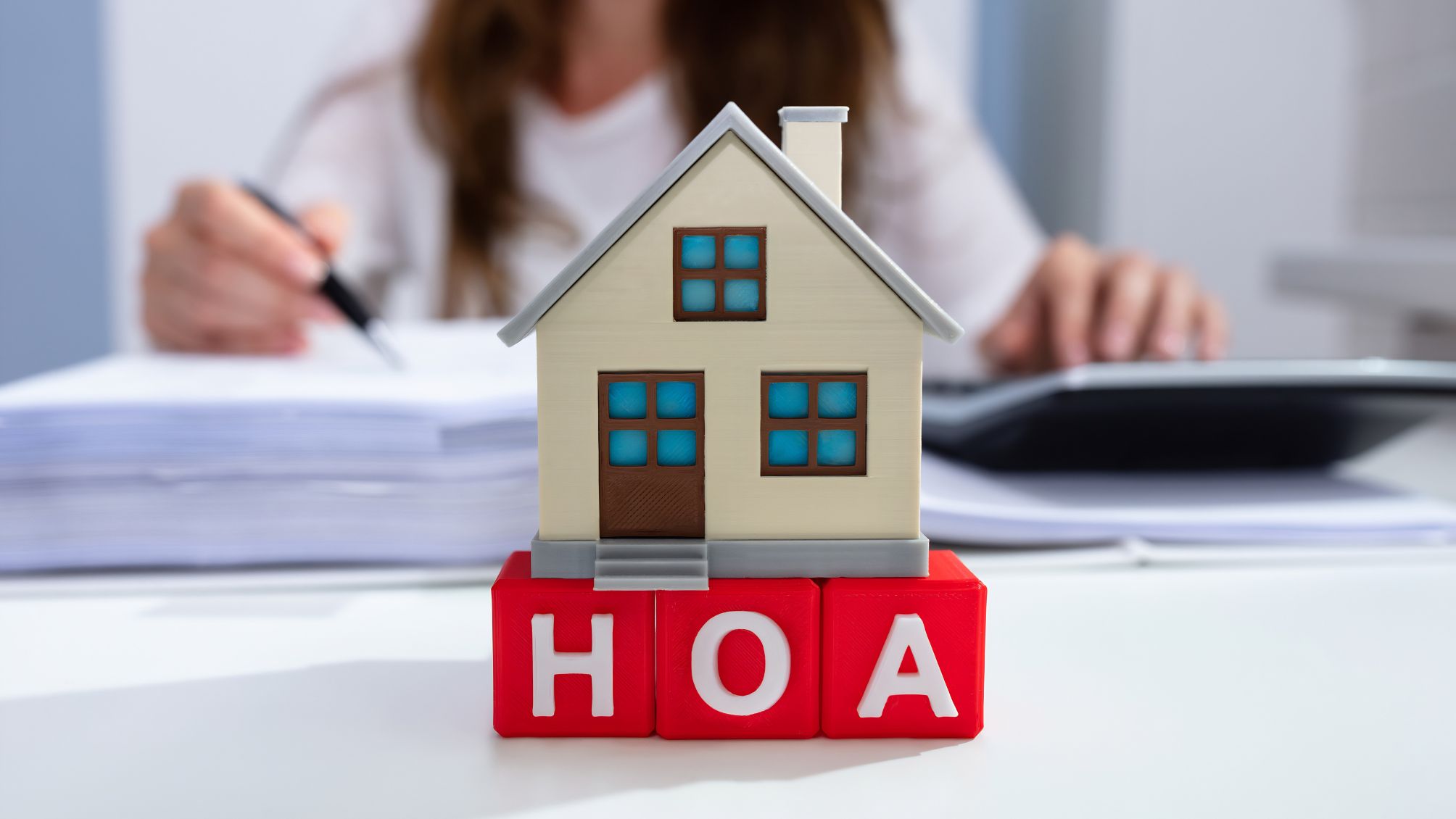 Close-up Of House Model Over HOA Blocks In Front Of Businesswoman