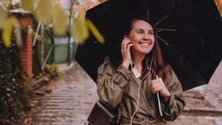 Woman listening to music through headphones while walking through the rain with umbrella