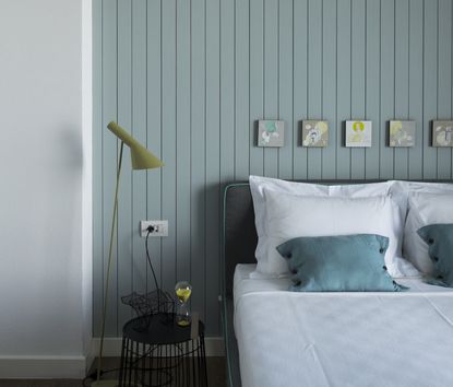 A bedroom with light blue wall paneling and a bed with white sheets and a floor lamp on the side