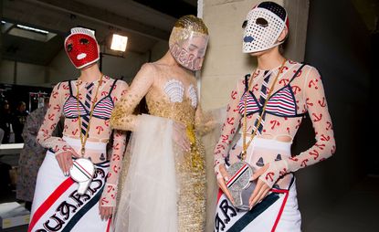 Models wear anchor printed tops with white skirts, and gold dress with shell bra and masks