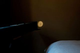 Black object focused on a small moon-shaped image in a dark room