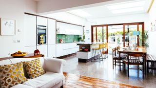 a bright and light-filled kitchen extension with kitchen island, a wooden dining table, and a large white sofa in the living space