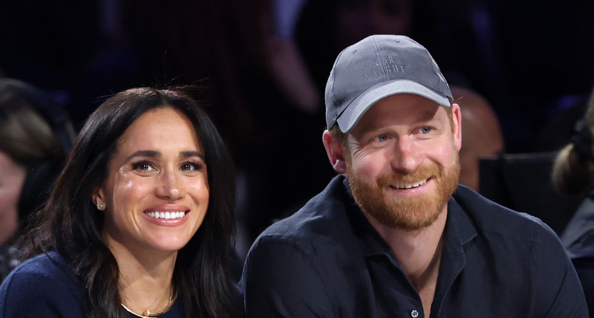 Prince Harry and Meghan Markle sitting next to each other at a basketball game and smiling